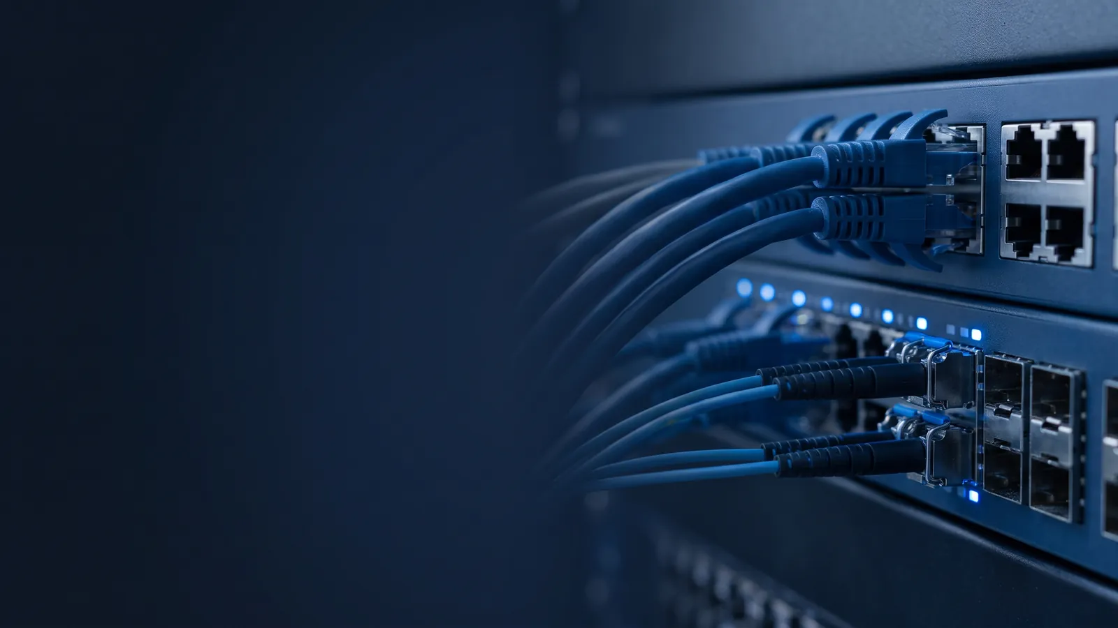 Netzwerk-Switch im Server-Rack mit gesteckten blauen Patchkabeln und Glasfaserleitungen